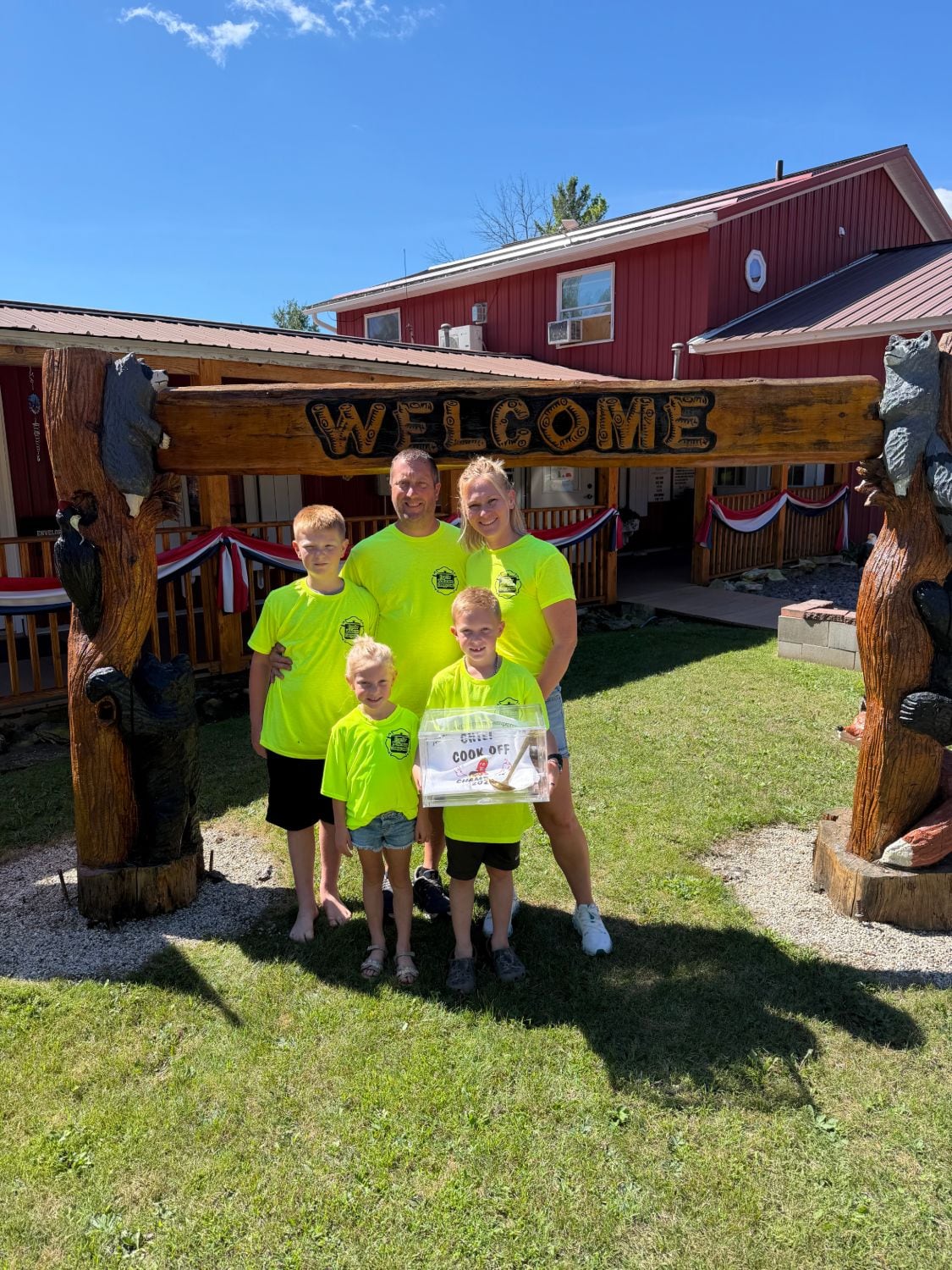 Todd, Cara, and the kids under the hand-carved welcome arch, holding the chili cook-off champion trophy