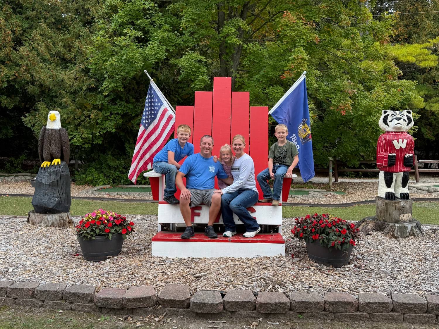 The Rasmussen family on the oversized red FWC Adirondack chair, flanked by the carved eagle and Bucky Badger
